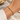 A gold cable-wrapped bracelet with a polished link clasp, shown worn on a person's wrist.