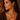 A woman in a brown knit sweater wearing a gold heart tiger's eye gemstone pendant necklace and matching large hoop earrings.