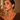 A close-up of a woman wearing large gold geometric triangle hoop earrings with a hinged clasp.