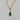 A gold chain necklace with a marquise-shaped pendant featuring a green jade gemstone, set against a light gray marble background.