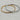 Two slim bangle bracelets overlapping on a light marble surface. One bracelet is yellow gold with small clear stones set along the front, and the other is silver with matching clear stones.